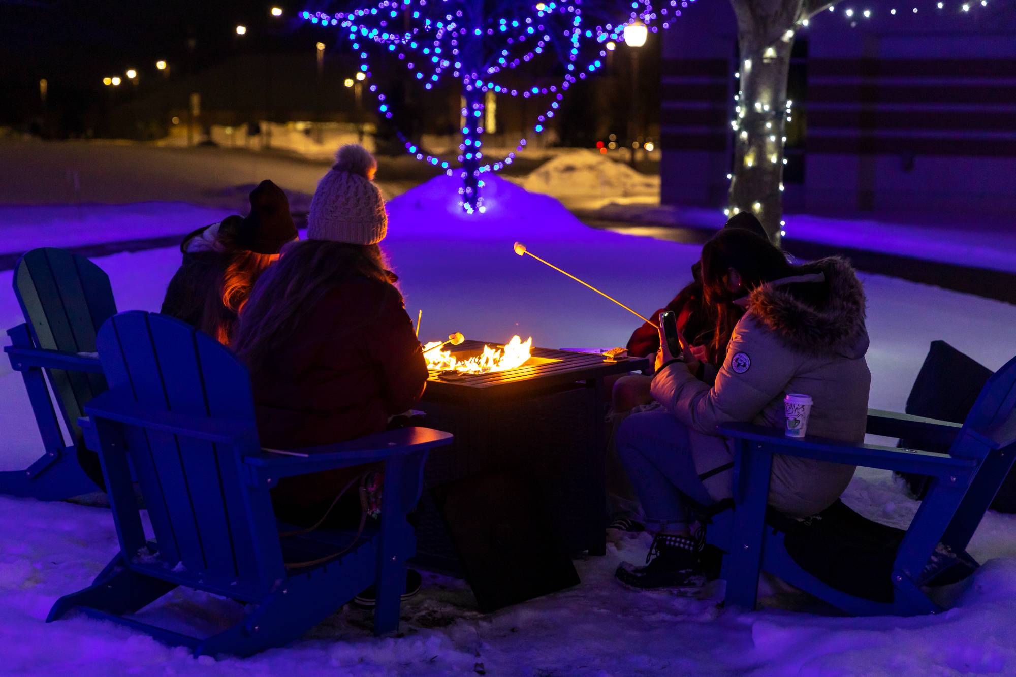 GVSU students roasting marshmallows around a fire together in the winter